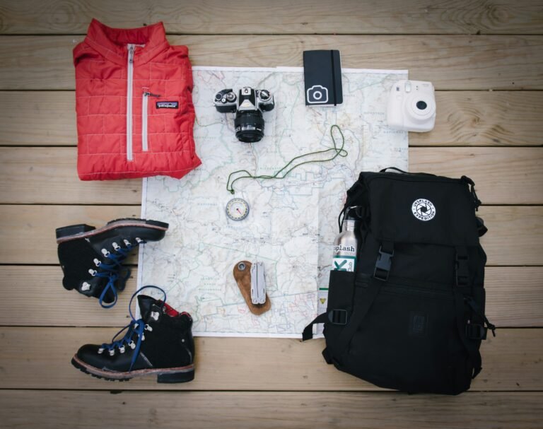 black-hiking-backpack-near-white-fujifilm-instax-mini-camera-near-black-leather-boots-red-half-zip-jacket-gray-pocket-watch-on-white-map